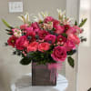 Pink roses and lilies arranged in a square box with a pink ribbon