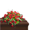 Red rose casket spray with greenery on a wooden casket