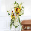 Tall funeral spray of yellow, red, and white flowers with a ribbon on an easel
