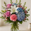 Bouquet of pink roses, blue hydrangeas, white lily, and pink carnations in a glass vase