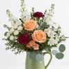 Peach roses and white flowers arranged in a green ceramic pitcher