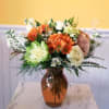 Orange and white flower arrangement in an amber glass vase