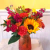 Colorful mixed bouquet in an amber glass vase with a sunflower and roses