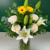 White lilies and cream roses in a glass vase with yellow flowers