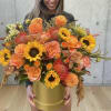 Large orange and yellow bouquet in a gold hatbox held by a woman