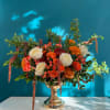 Mixed orange and white floral arrangement in a gold vase