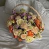 Basket of pastel roses, carnations, and purple blooms on white bedding