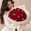 Woman holding a bouquet of red roses wrapped in white paper with a satin bow.