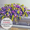 Large purple, green, and peach flower casket spray draped over a silver casket