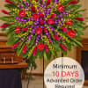 Large round tropical standing spray with red, purple, and yellow flowers on a metal easel in a funeral setting