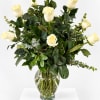 White roses in a clear glass vase with dark greenery