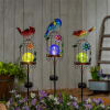 Three colorful bird garden stakes with glowing orb lights above purple flowers