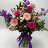 Mixed bouquet of pink and purple flowers in a glass vase with a purple ribbon