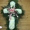 White floral cross arrangement with pink roses and ribbon on a wooden wall