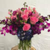 Pink roses and purple flowers arranged in a clear glass vase