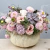 Low pastel arrangement of roses, dahlias, hydrangea and succulent in a white pumpkin container