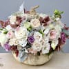 Pastel roses and orchids arranged in a white pumpkin container with a rope stem
