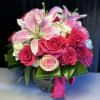 Pink lilies and roses arranged in a glass vase with a ribbon