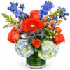 Bright mixed bouquet in a glass vase with orange, blue, and pale blooms