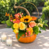 Pumpkin flower arrangement with sunflowers and roses in a basket handle
