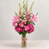 Pink lilies and roses in a clear glass vase with a ribbon