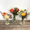 Three small flower arrangements in clear glass vases on a wooden surface
