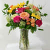 Mixed bouquet of pink, peach, and yellow flowers in a clear glass vase