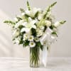 White lilies and daisies arranged in a clear glass vase with a white ribbon