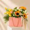 Pink gift bag filled with yellow tulips, sunflowers, and daisies