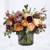 Mixed rose bouquet in a clear glass vase with peach, cream, purple, and orange blooms
