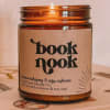 Amber glass candle jar with a lit wick and a paper label reading "book nook"