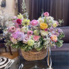 Mixed pastel flower arrangement in a wicker basket with ribbon ties