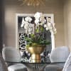 Tall white orchid arrangement in a gold bowl on a table