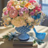 Pastel bouquet of roses, hydrangeas, and daisies in a blue vase with bird accents