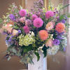 Large pastel bouquet in a white vase with pink, purple, peach, and green blooms