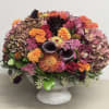 Mixed floral arrangement in a gray pedestal vase with pink, orange, and dark blooms