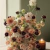 Tall bouquet of peach, blush, white, and burgundy flowers beside a lit candle