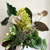 Tropical arrangement with yellow orchids and large glossy leaves in a white vase