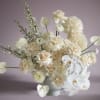 Cream and white floral arrangement in a white vase with orchids and roses
