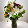 Bouquet of white lilies, roses, and purple flowers in a glass vase