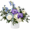 White and blue floral arrangement with purple orchids in a white vase