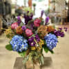 Colorful bouquet with blue hydrangeas, pink roses, and purple flowers in a glass vase