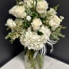 White roses and hydrangeas in a glass vase with a striped ribbon