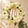 Cream floral wreath on a wooden easel with trailing greenery