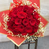 Round bouquet of red roses with white filler flowers wrapped in red and gold paper.