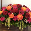 Low rectangular arrangement of red, orange, and hot pink roses in a wooden box
