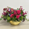 Low arrangement of hot pink roses and mixed purple flowers in a hammered gold bowl.