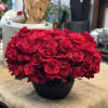 Low arrangement of many red roses densely packed in a glossy black bowl.