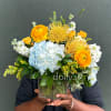 Mixed bouquet in a clear glass vase with blue hydrangea, orange blooms, and white flowers