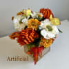 Artificial bouquet of orange, white, and yellow flowers in a square vase